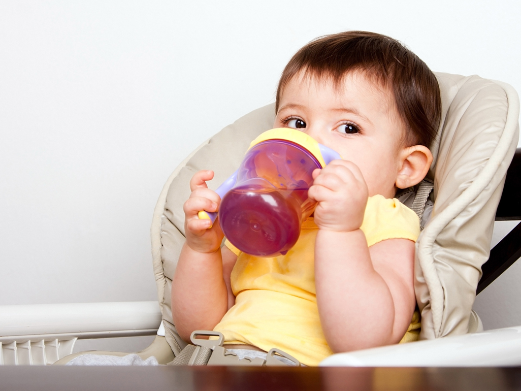 baby in a highchair drinking from a sippy cup