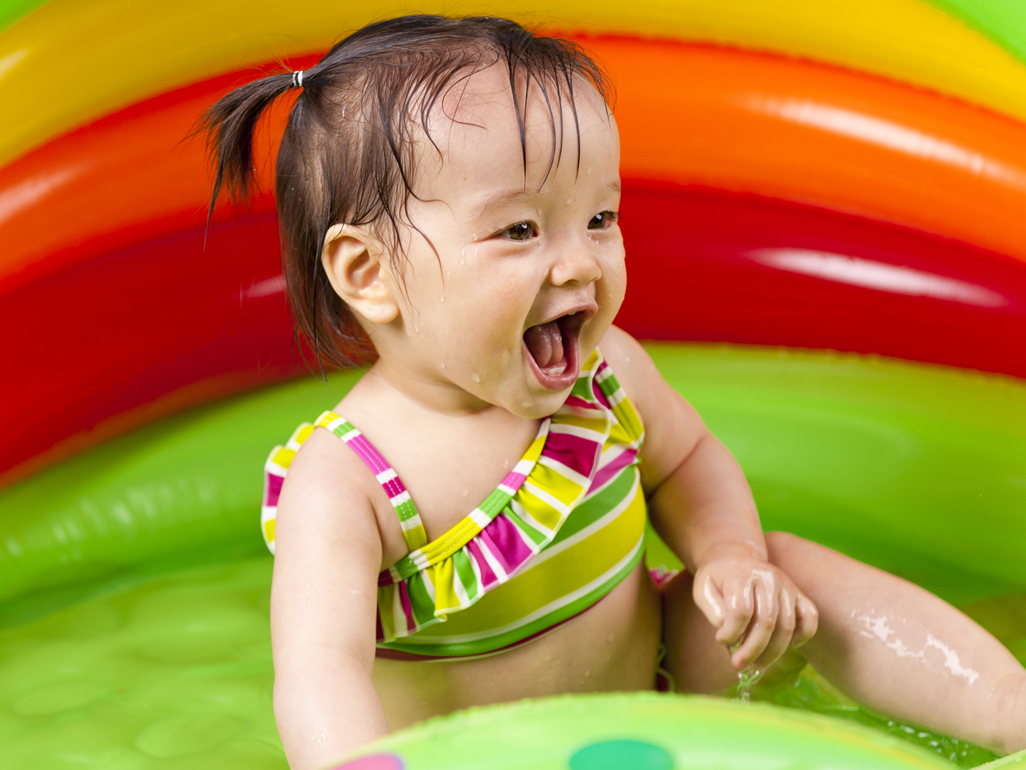 baby girl in colourful swimsuit plays in a paddling pool