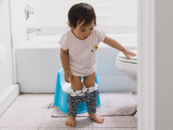 Child standing next to the toilet and potty in the bathroom with their trousers down.