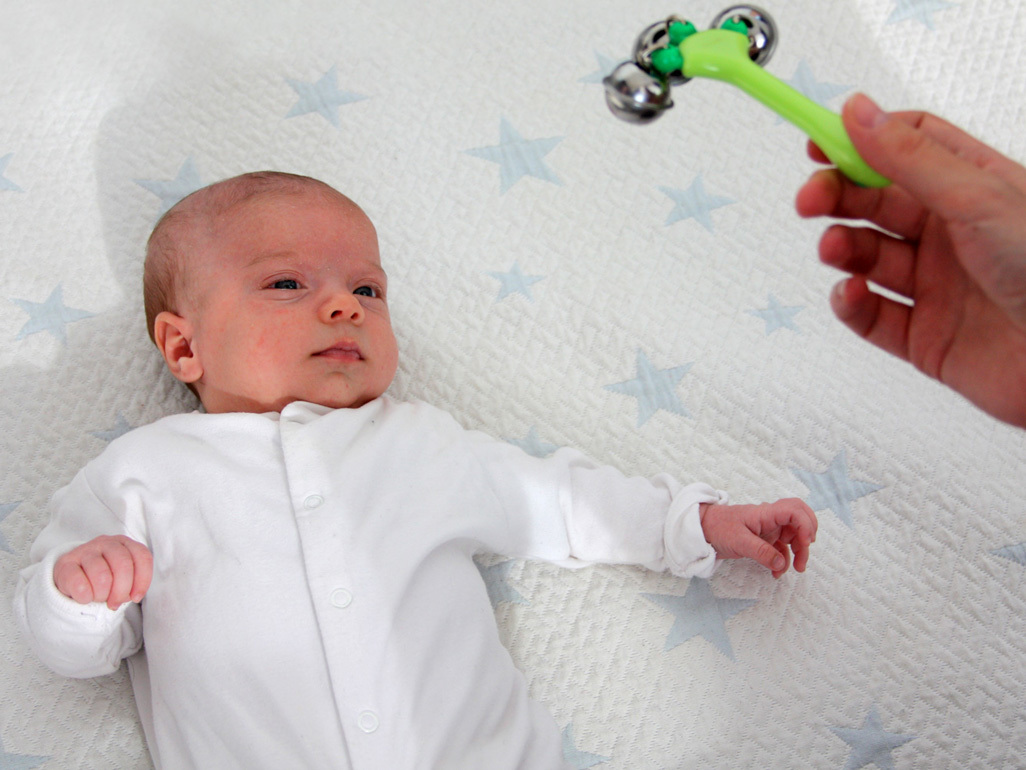 One month old baby lying on a blanket looking at a rattle