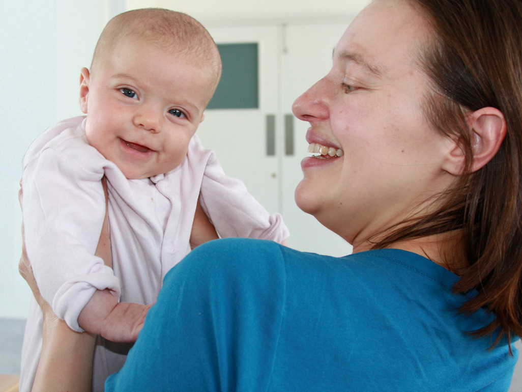 Two month old baby smiling over mum's shoulder