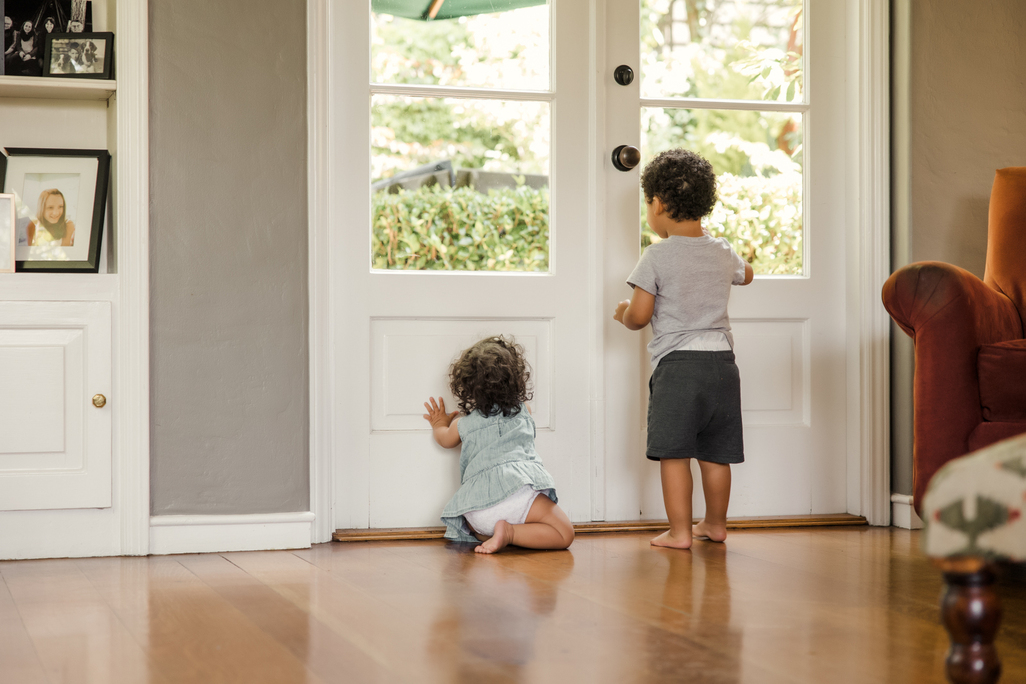 Big brother and baby sister playing by a windowed door