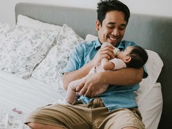 Dad bottle feeding their baby formula while laying down on the bed