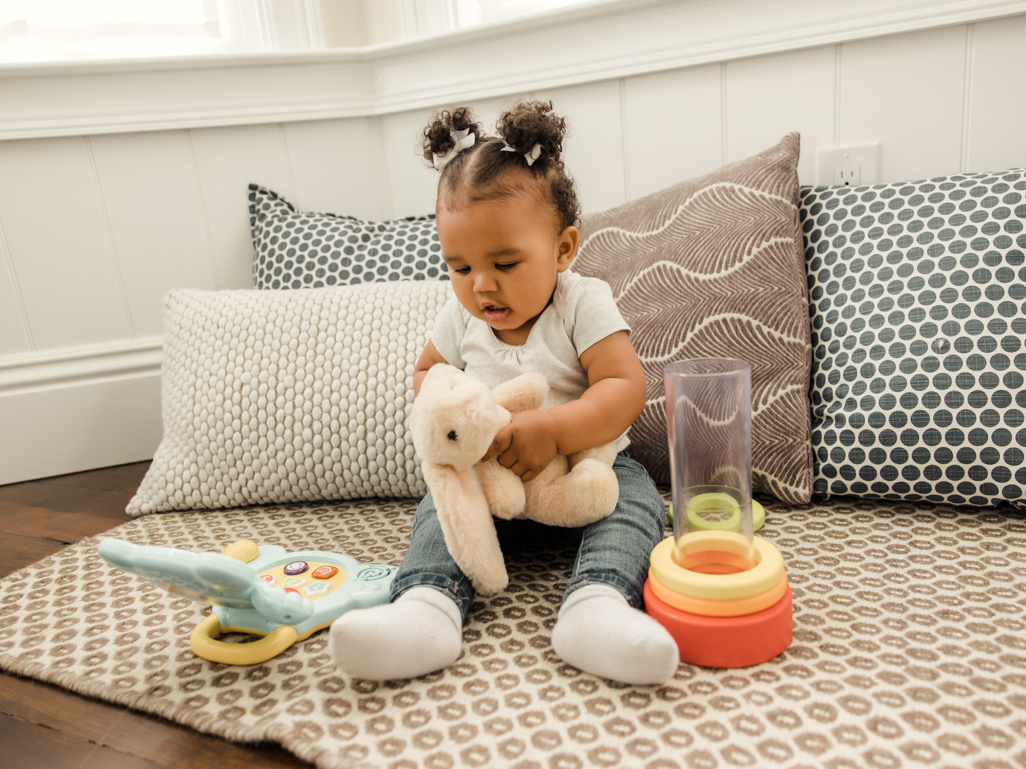 Baby girl sat on a rug playing with toys