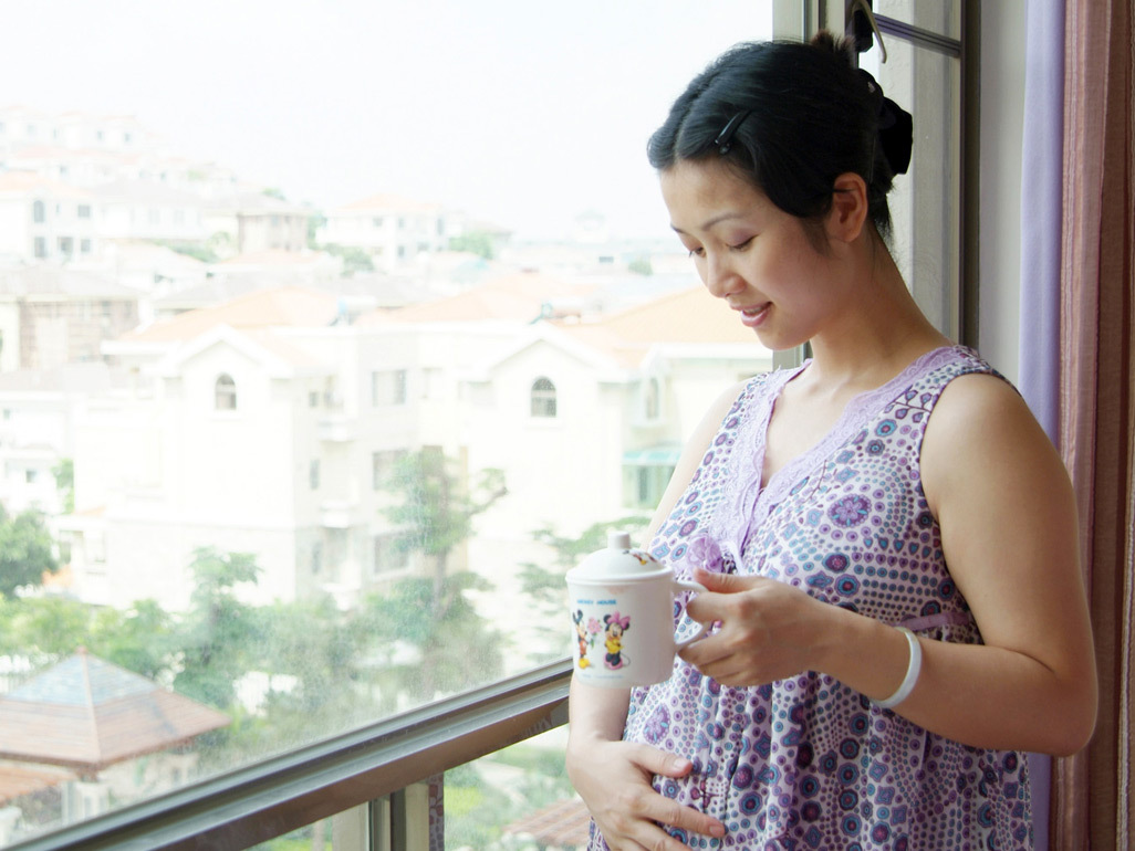 Pregnant woman standing on a balcony and looking at her bump