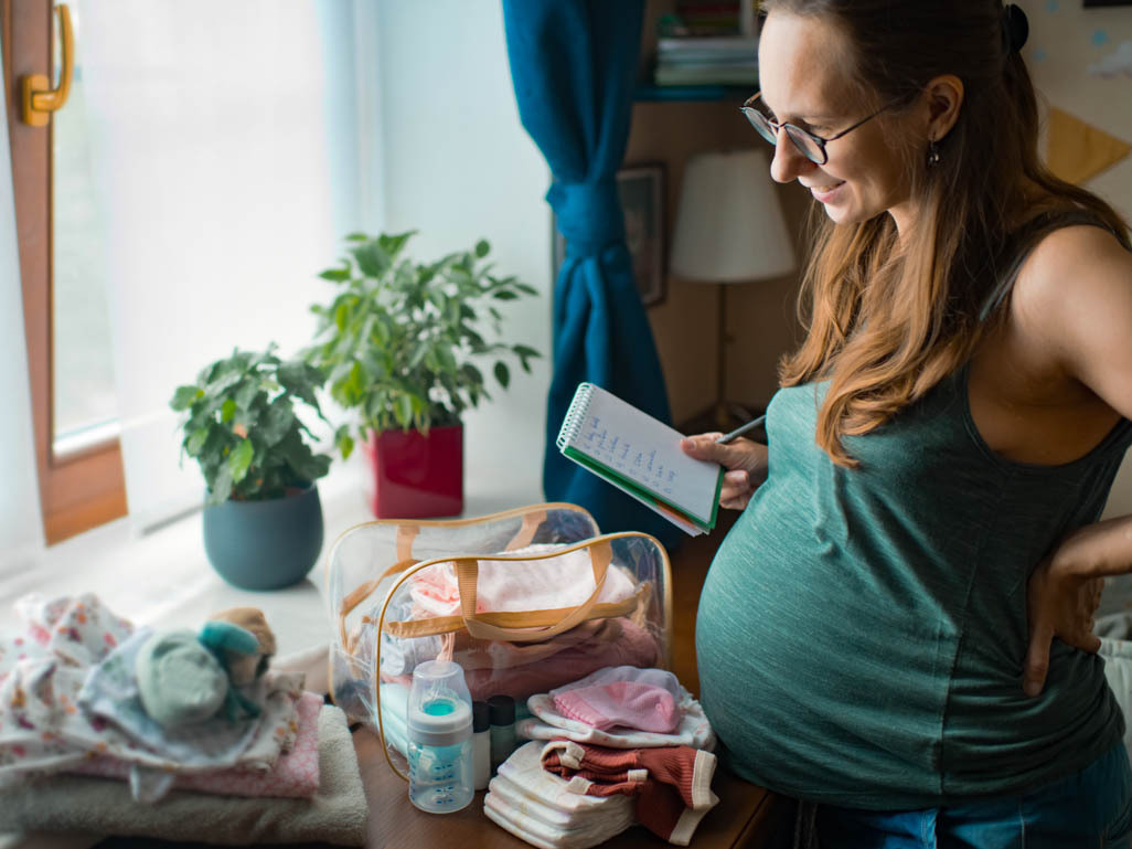 Pregnant woman writing in notepad next to a suitcase