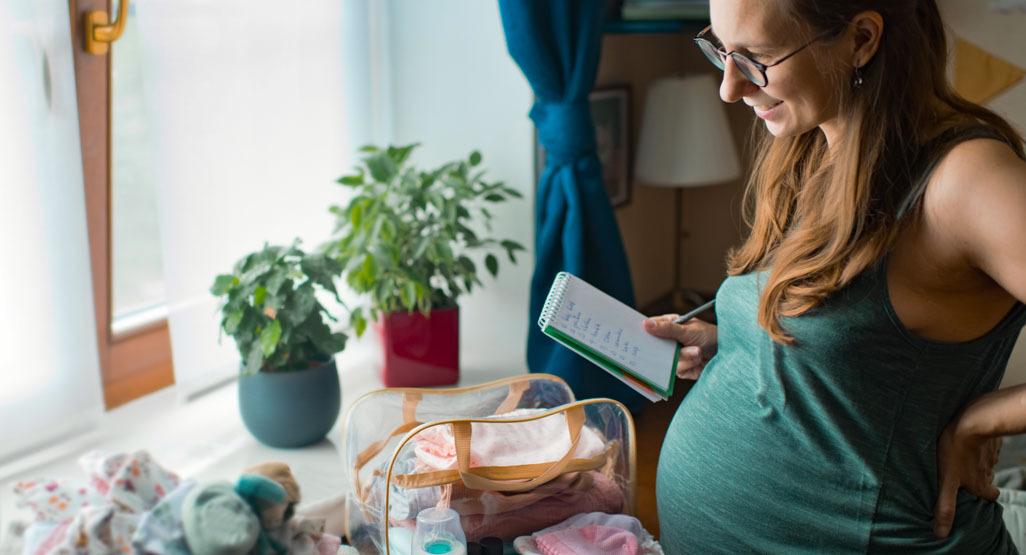 Pregnant woman writing in notepad next to a suitcase