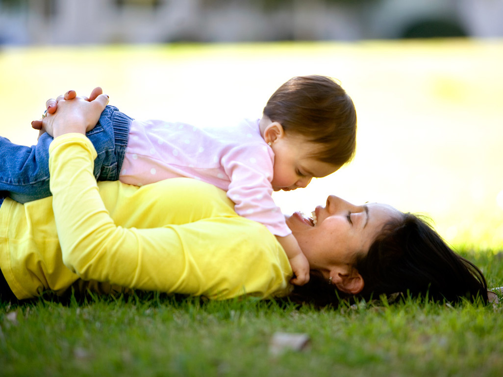 Smiling mother lying in green grass with her baby on her chest
