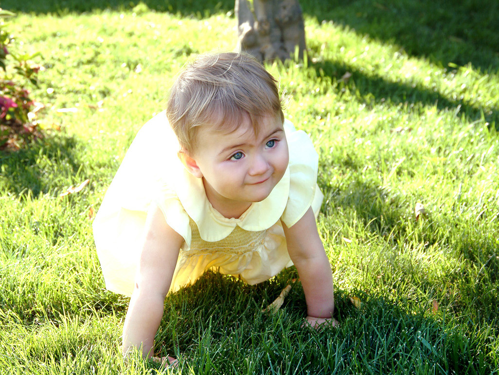 baby girl in yellow dress crawling across lawn
