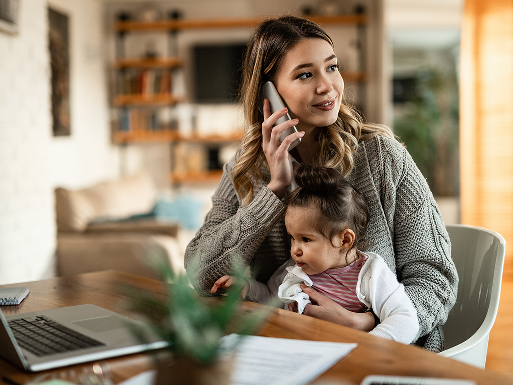 Mother on the phone working from a laptop with a baby on her lap 