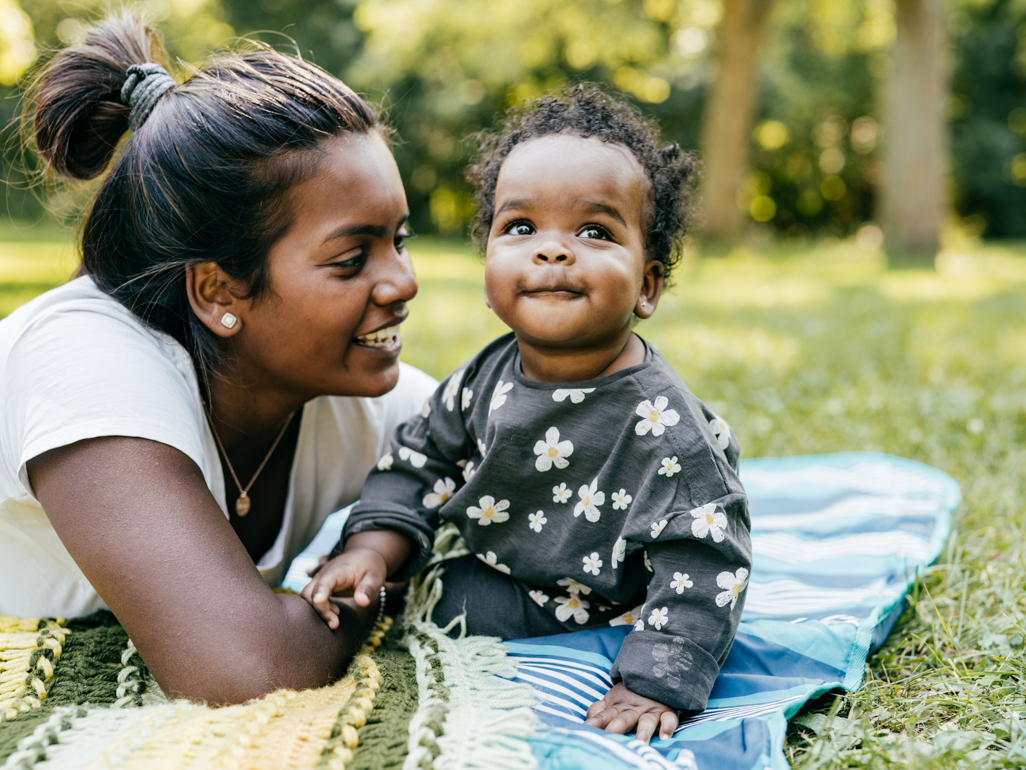 A mother and baby sitting on a blanket in the grass