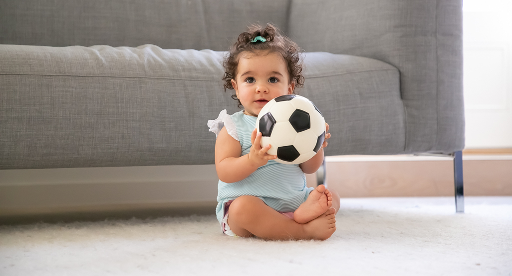 Toddler girl sitting by sofa holding football