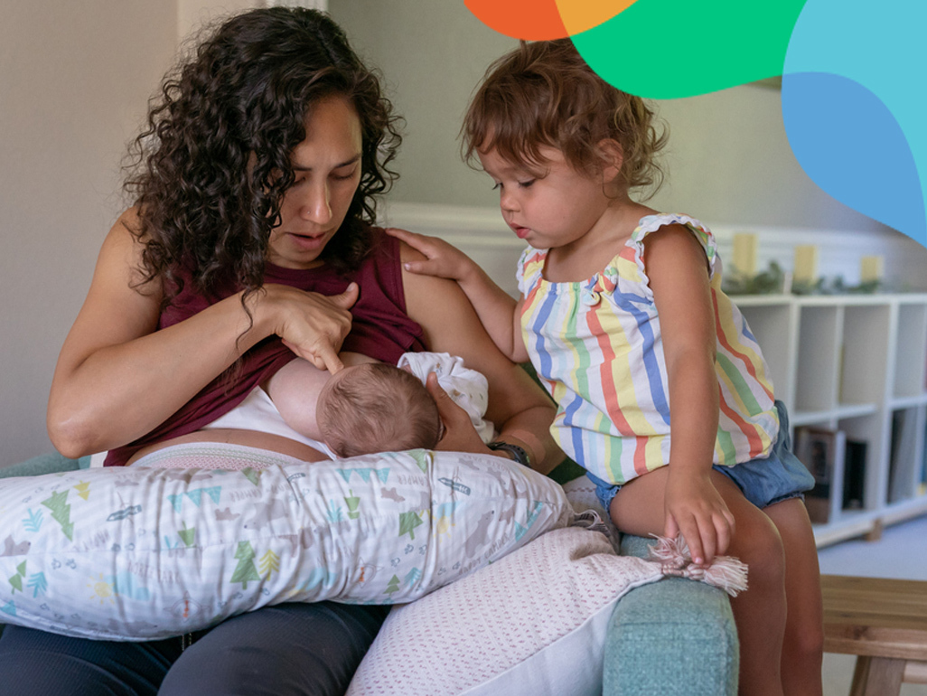 Mum breastfeeding her baby on the sofa with young child watching