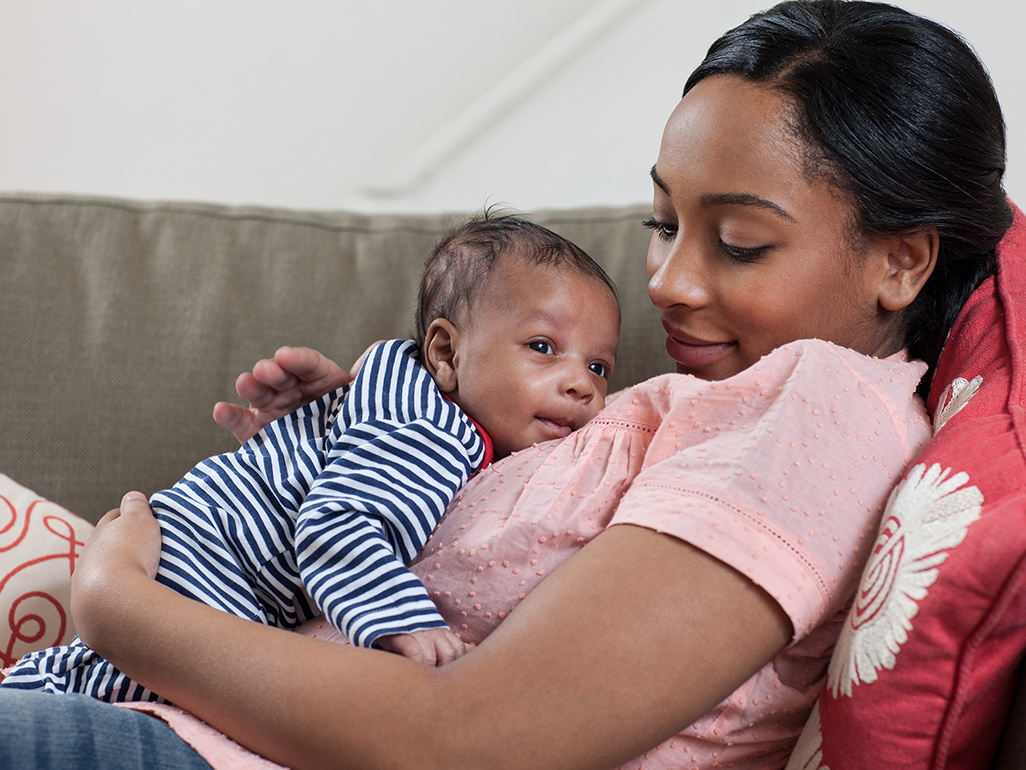 A mother lays back on a sofa holding her baby to her chest