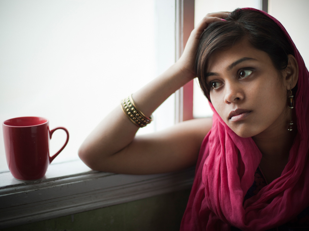 Pregnant woman resting elbow on window sill and looking out of the window with a worried expression