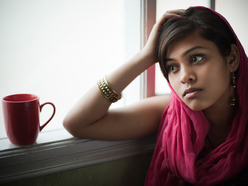 Pregnant woman resting elbow on window sill and looking out of the window with a worried expression