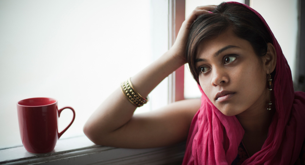 Pregnant woman resting elbow on window sill and looking out of the window with a worried expression