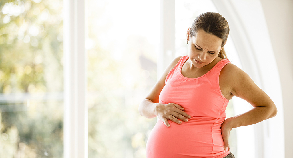 Woman in early labour rubbing her back and belly
