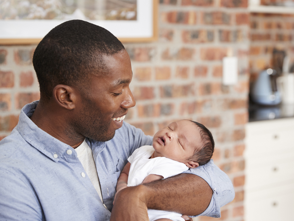 A dad holding a newborn baby while smiling