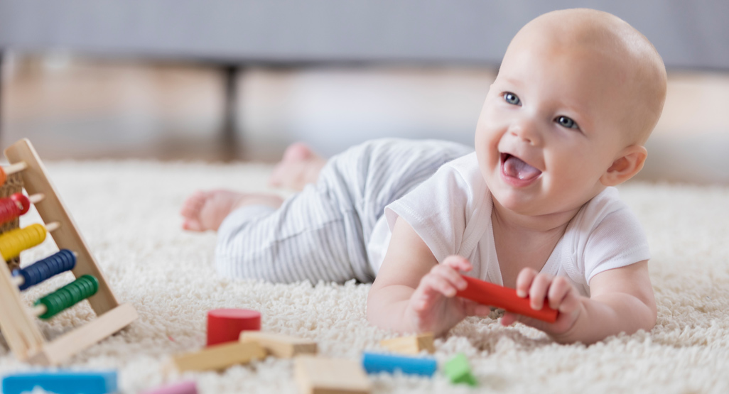 Baby playing and smiling on rug with toys