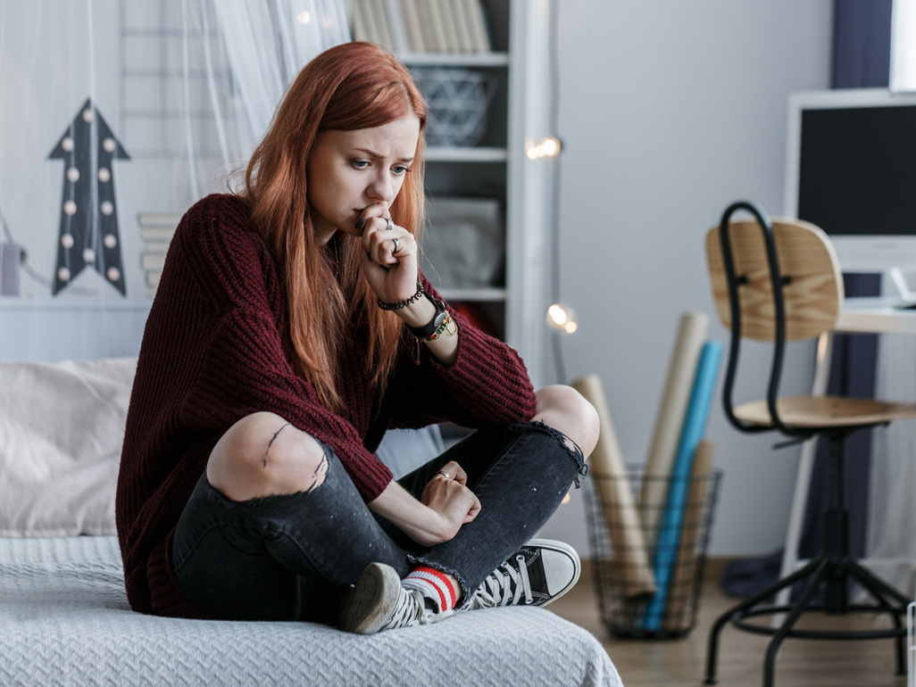 Stressed woman sat cross-legged on her bed 