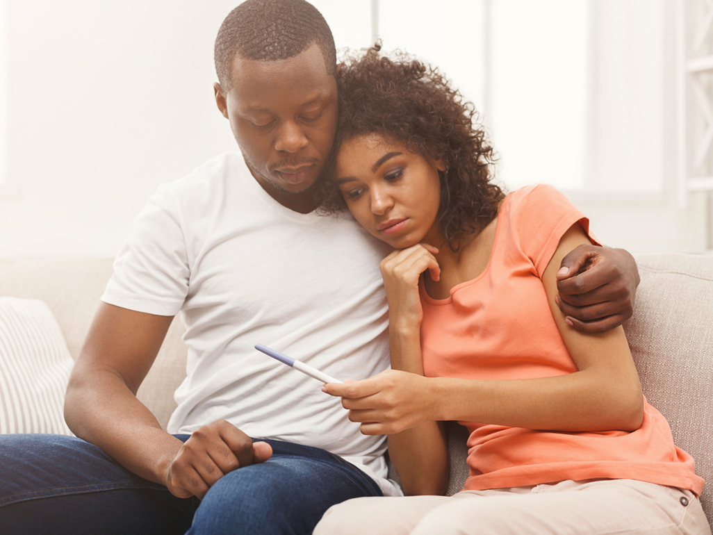 Couple sitting on a sofa looking sadly at a negative pregnancy test
