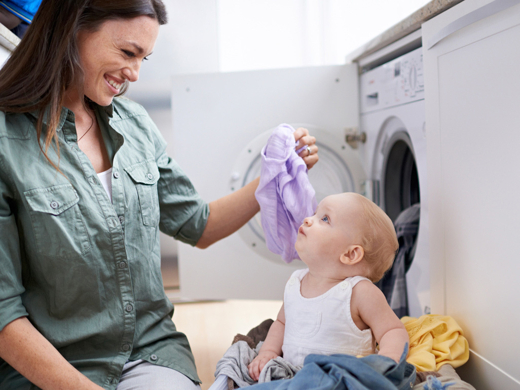 A baby sits in a washing basket looking at her mum