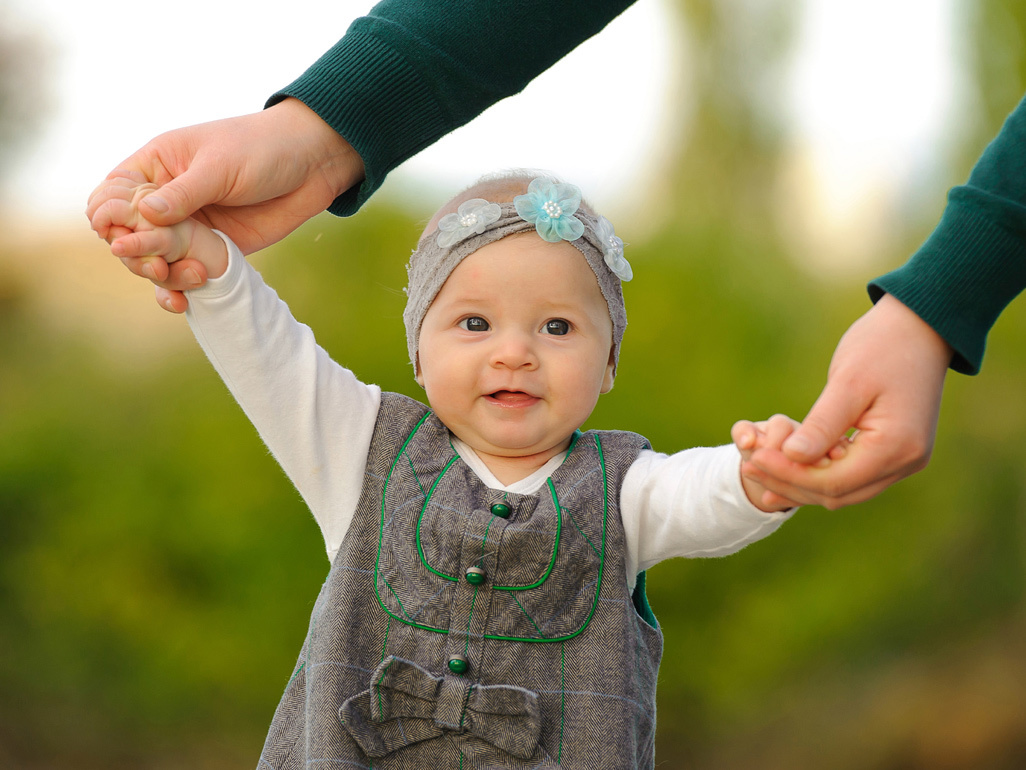 Mum helps baby daughter to stand by holding her hands