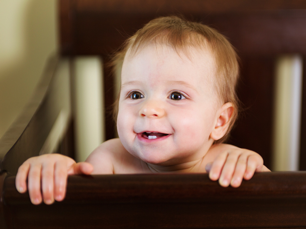 baby boy holding the sides of his wooden crib