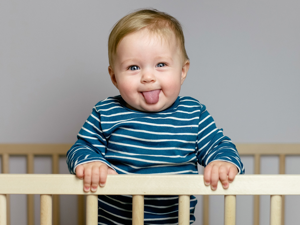 baby boy in blue and white stripped top pokes out his tongue