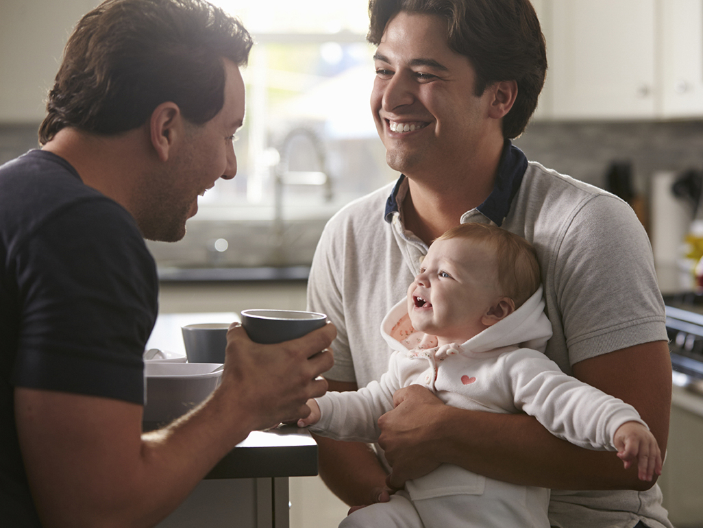 Two dads laughing with baby on his lap