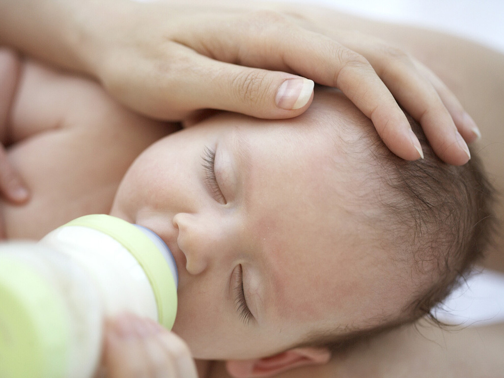 Mother caressing her young baby as she gives formula milk in a bottle