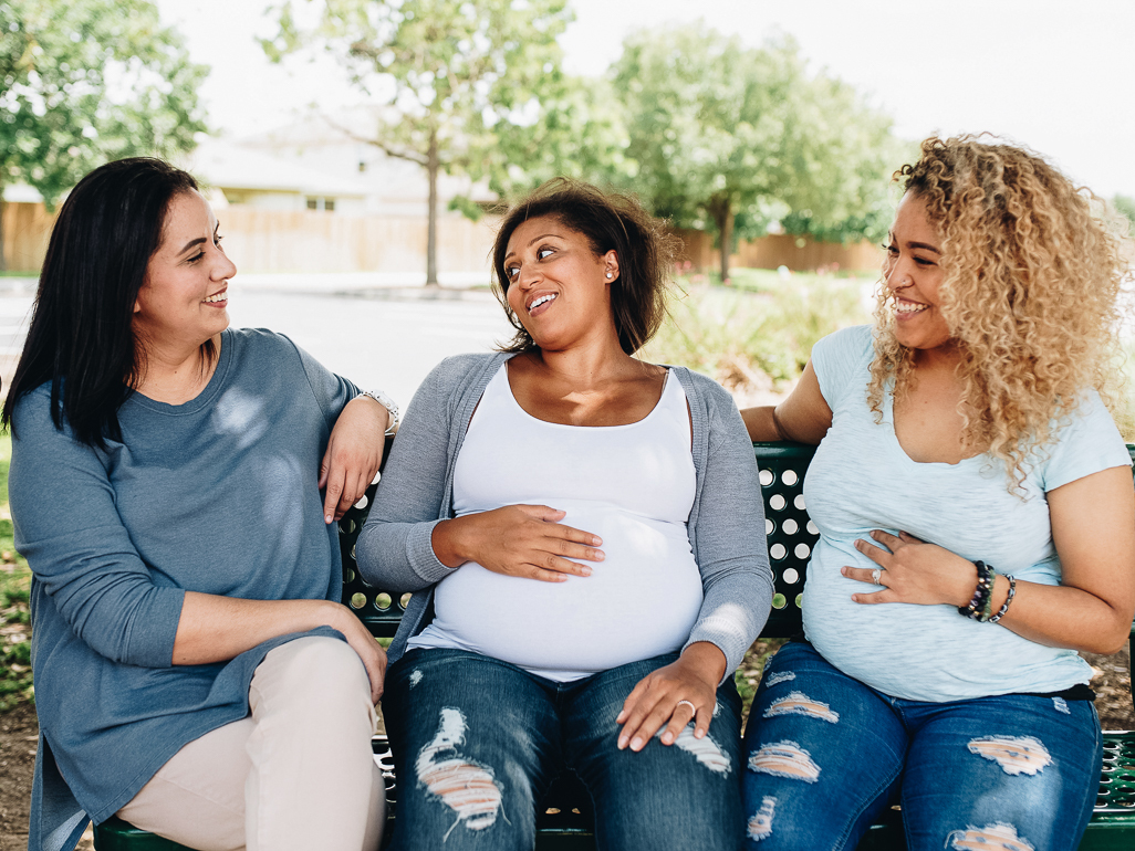 Pregnant woman sitting on a bench with two pregnant friends