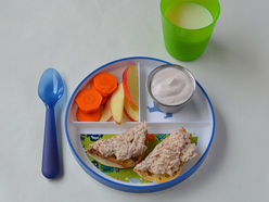 Three-sectioned plate filled with tuna on toast, carrots, slices of apple and a pot of yoghurt.