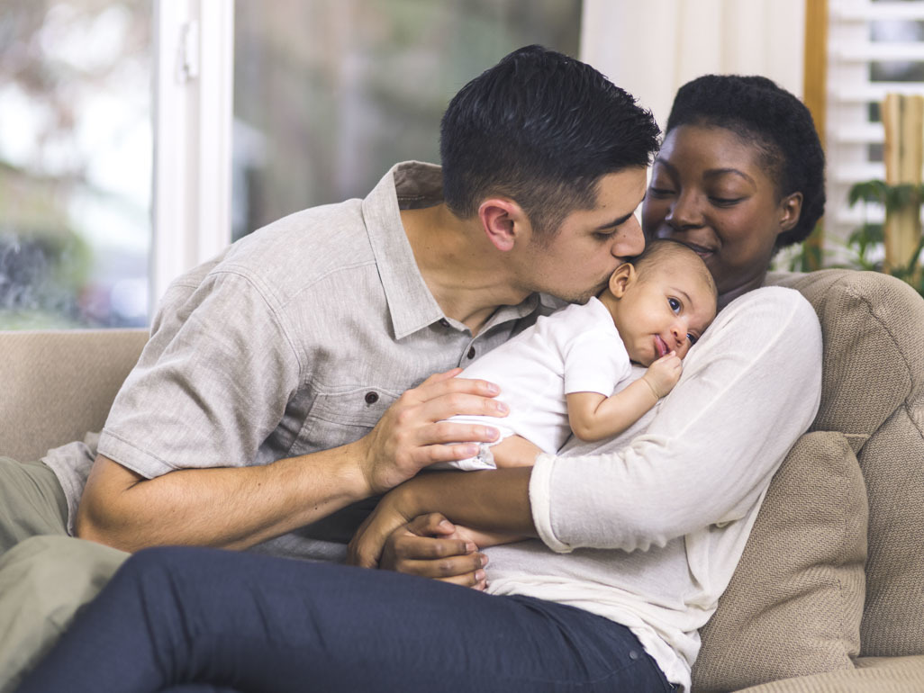 A dad kisses a newborn that a mum is holding to her chest