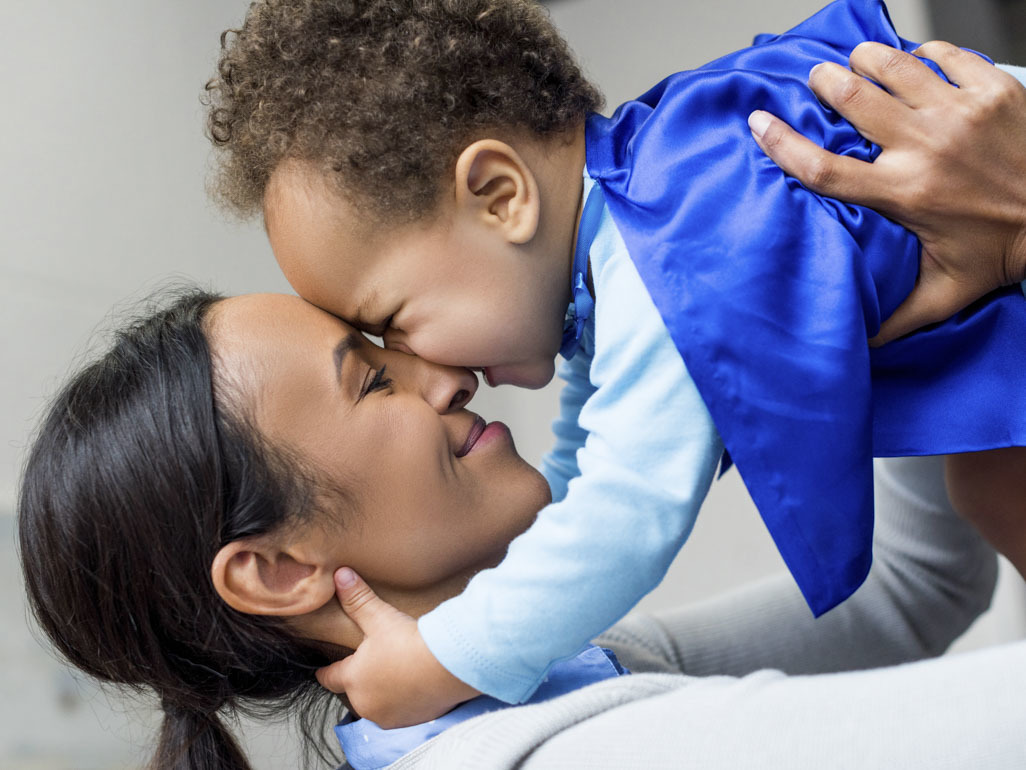 A mum holding baby wearing a super hero cape
