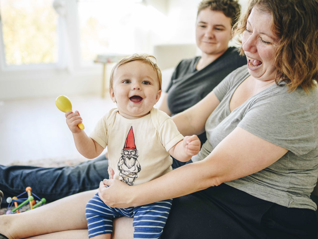Two mums laughing with a baby holding a rattle